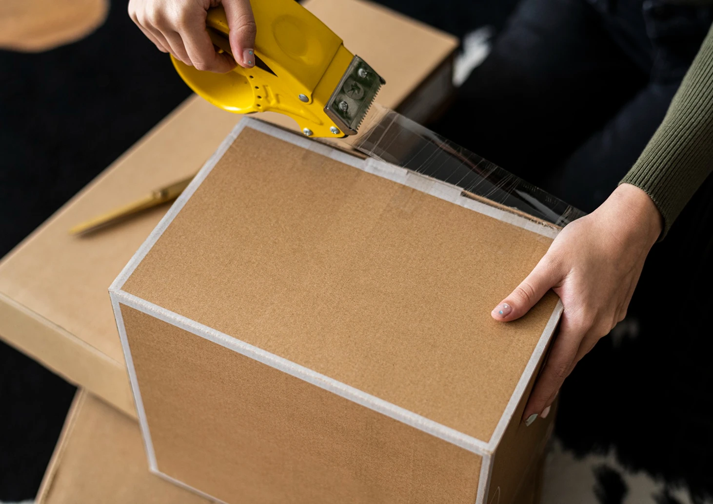 Person sealing cardboard package with tape for safe parcel delivery guidelines